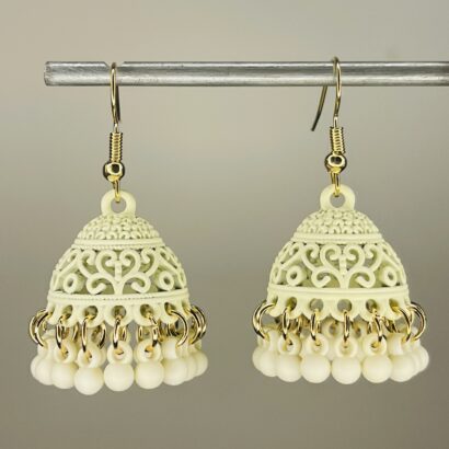 Pair of handcrafted cream color jhumka earrings with intricate floral design and dangling pink beads, featuring golden hooks and no golden bead detailing.