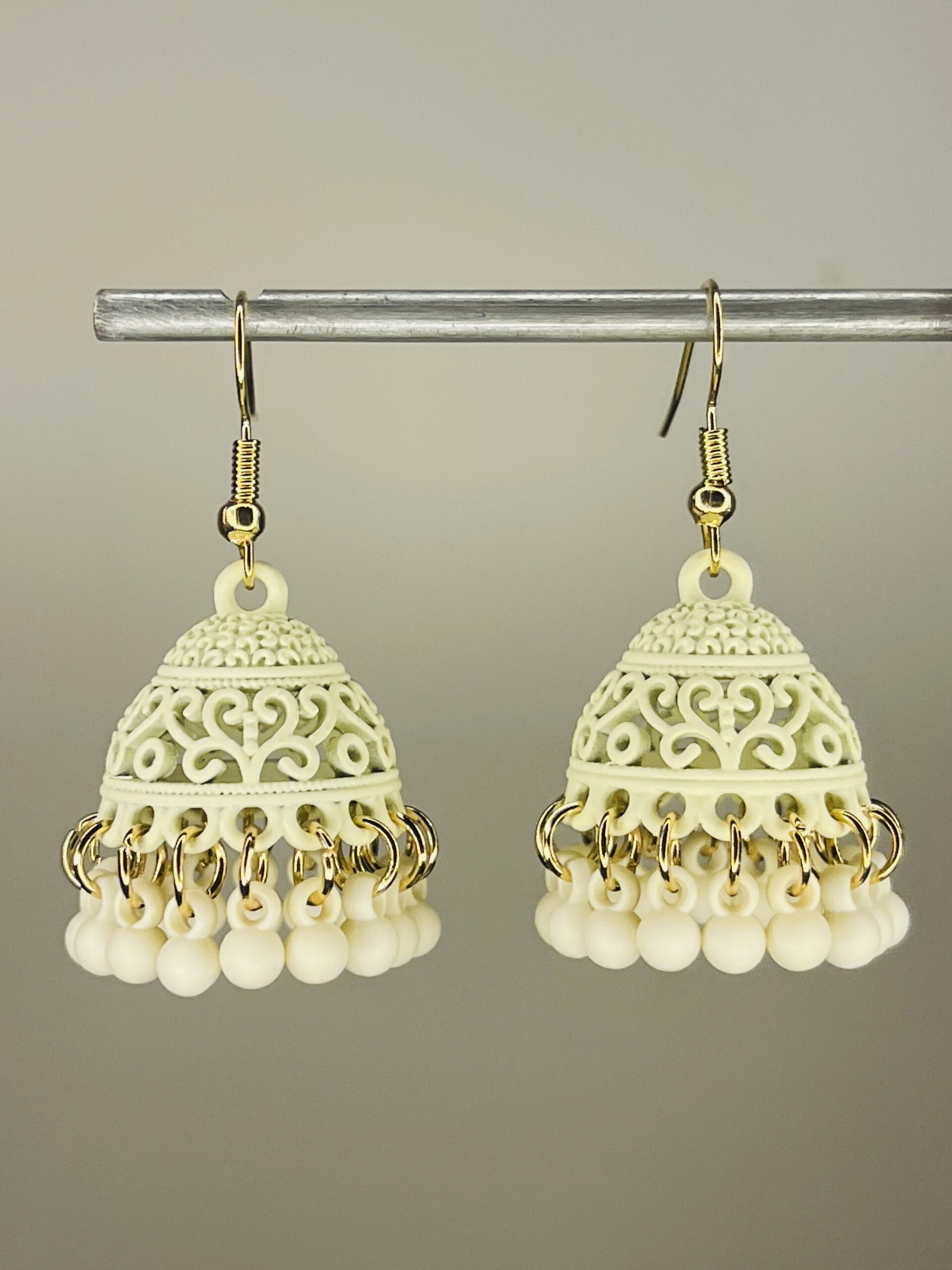 CREAM Pair of handcrafted cream color jhumka earrings with intricate floral design and dangling pink beads, featuring golden hooks and no golden bead detailing.