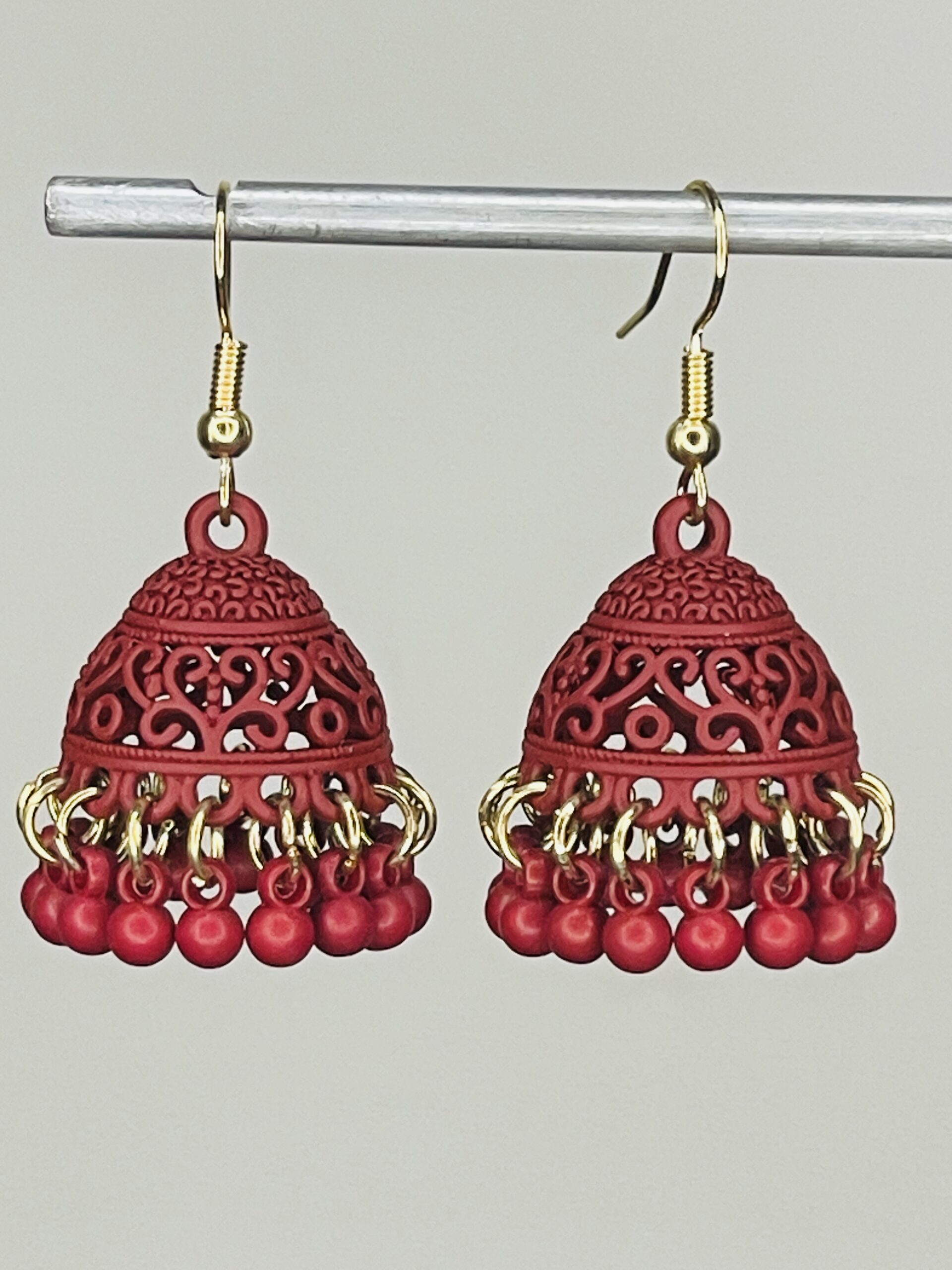 Pair of handcrafted light maroon jhumka earrings with intricate floral design and dangling pink beads, featuring golden hooks and no golden bead detailing.