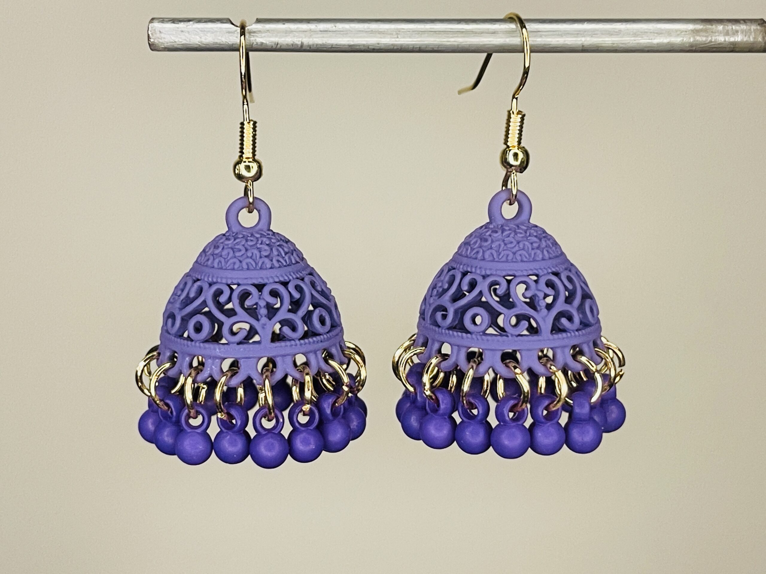 Pair of handcrafted lavender jhumka earrings with intricate floral design and dangling pink beads, featuring golden hooks and no golden bead detailing.